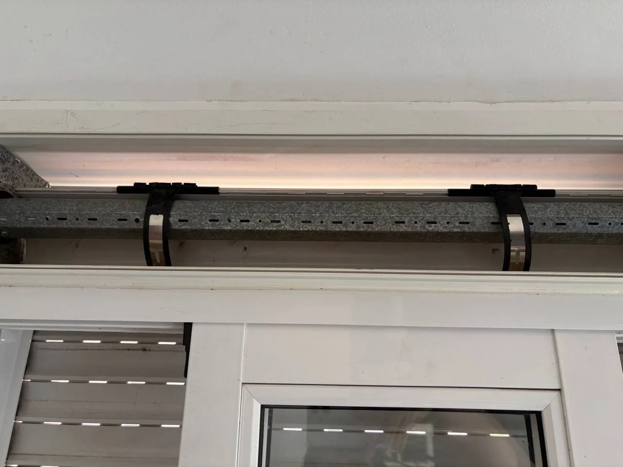Two new black roller-shutter hangers installed across the galvanized roller tube